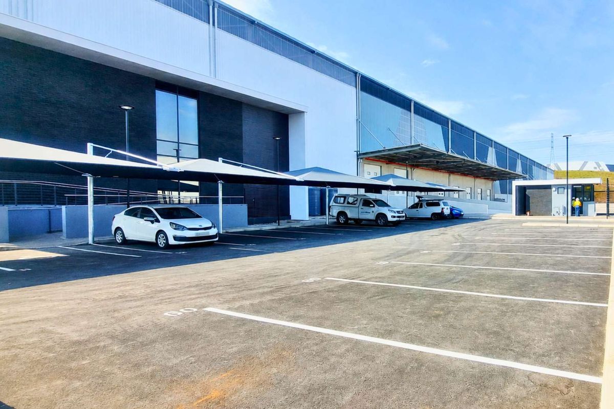 Modern industrial facility featuring a paved parking area with shade cloth carports and a large warehouse structure with a loading bay.