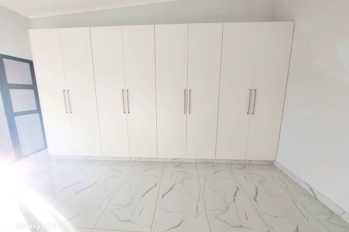 A bright bedroom featuring modern white built-in cupboards and contemporary marble-look floor tiles.