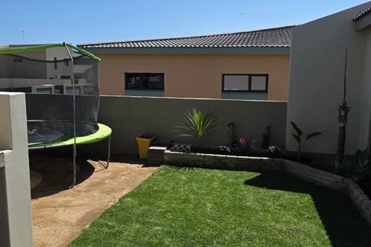 A private rear garden featuring a tiled patio area, a well-maintained lawn, and a low-level retaining wall with established garden beds.