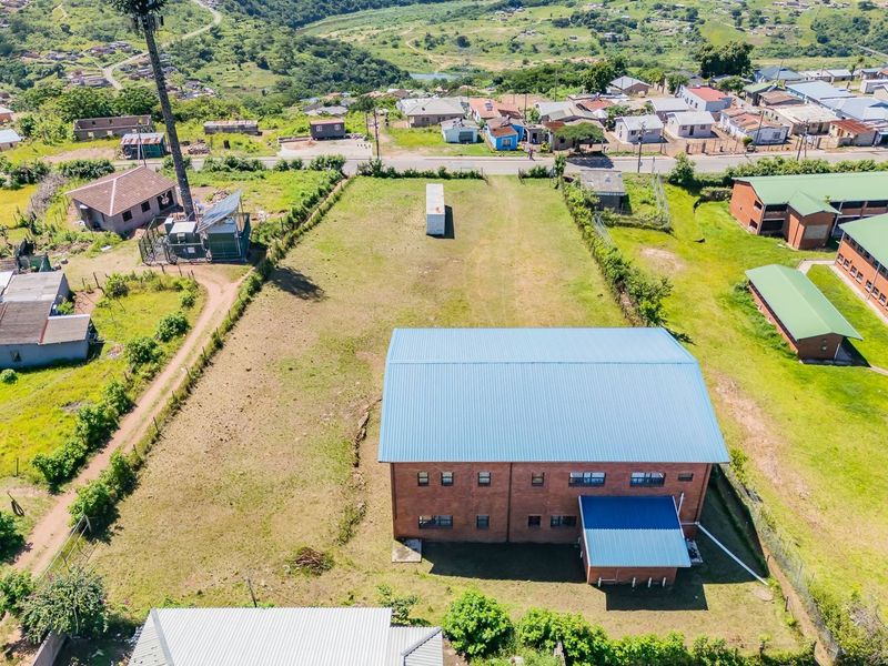 Aerial view of a residential plot featuring a large brick building with a metal roof, situated in a developed neighborhood.