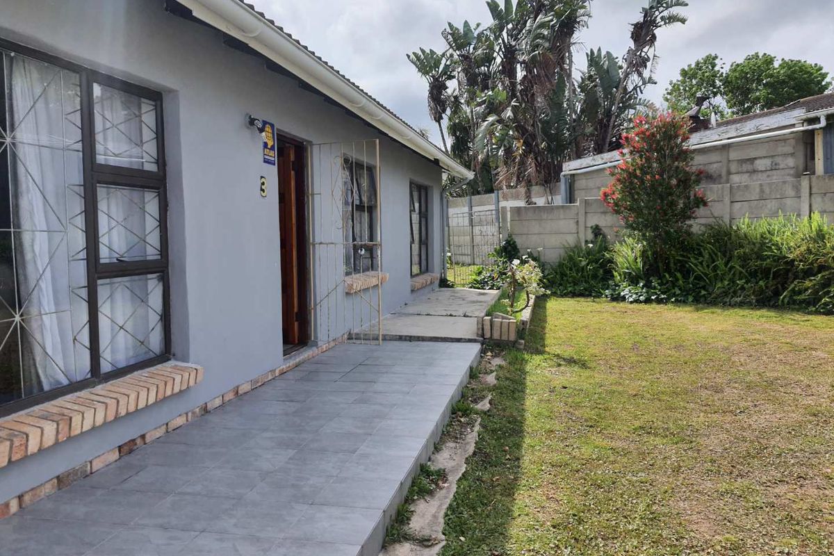 A side view of the house featuring a tiled walkway, security gates on windows, and a well-maintained garden area with perimeter walling.