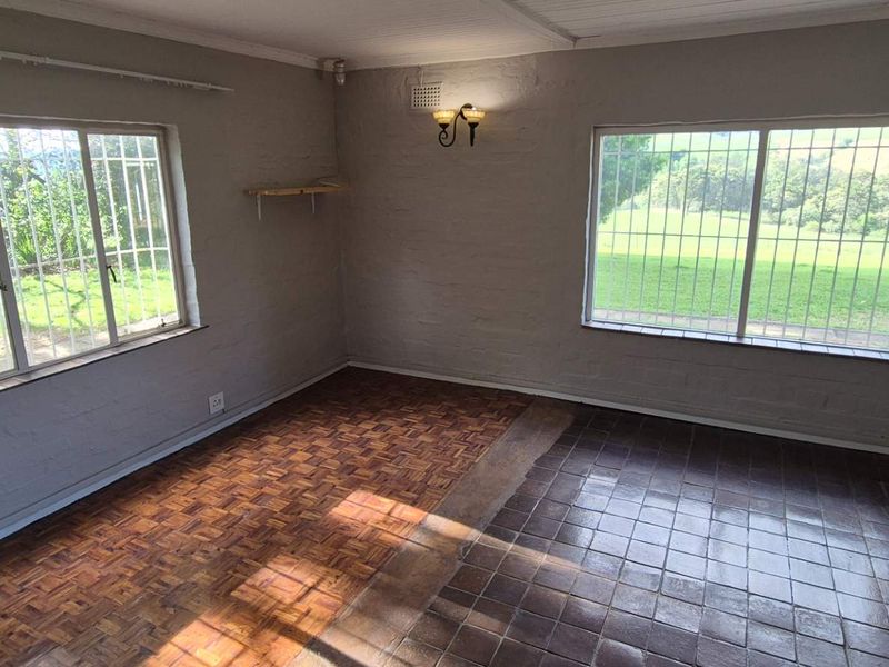 An empty living area featuring a mix of parquet and ceramic tile flooring, painted brick walls, and large windows with security bars.