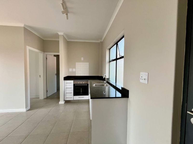 A clean, modern kitchen featuring granite countertops, built-in oven, hob, stainless steel sink, and neutral tiled flooring in an open-plan layout.