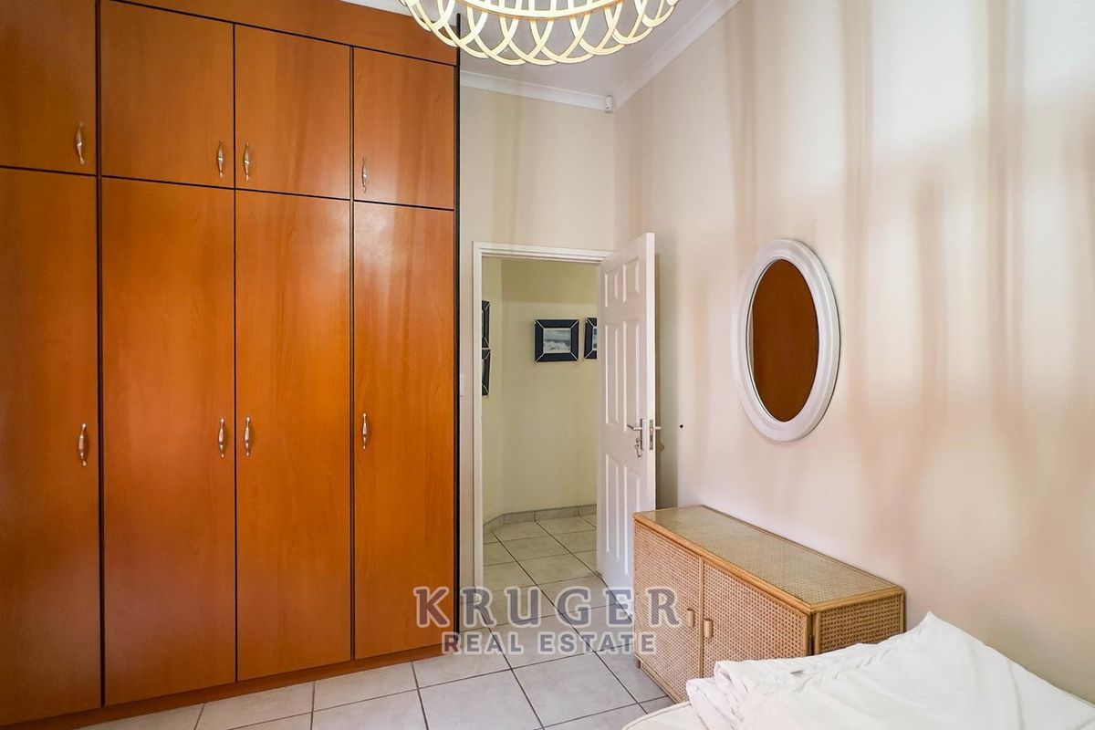 A bedroom featuring floor-to-ceiling built-in wooden cupboards, tiled flooring, and a doorway leading to an adjacent hallway.