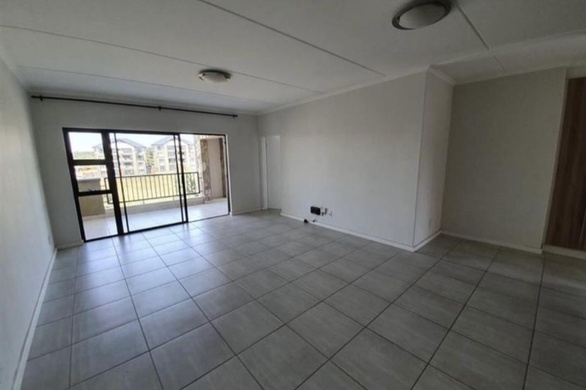 An empty, open-plan living area featuring neutral tiled flooring and a large sliding glass door providing access to an outdoor balcony.