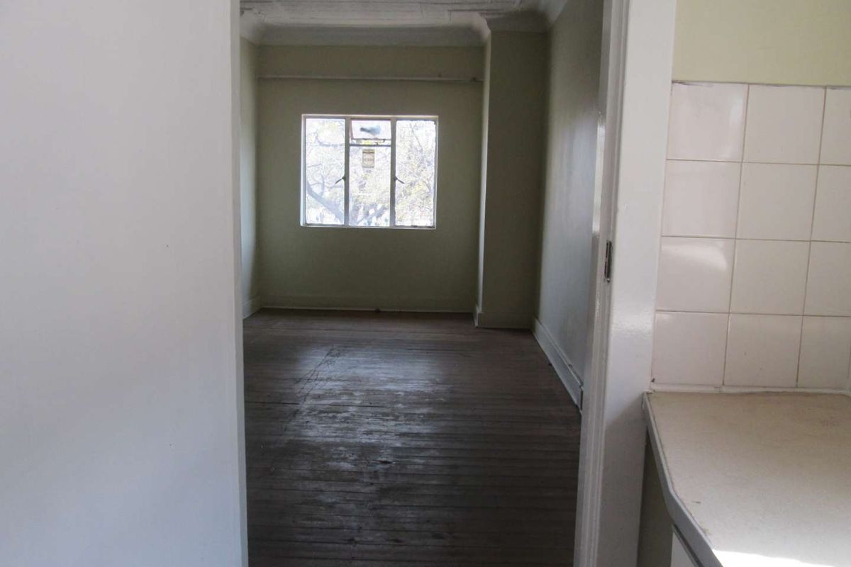 An empty bedroom featuring original timber flooring, decorative ceiling cornicing, and a window providing natural light.