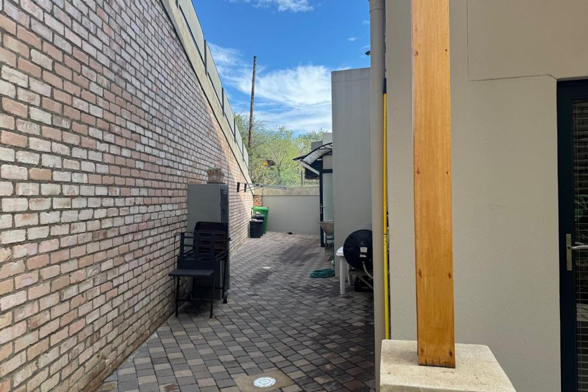 A paved side courtyard or utility area featuring a brick boundary wall, timber support post, and direct access to the main dwelling.