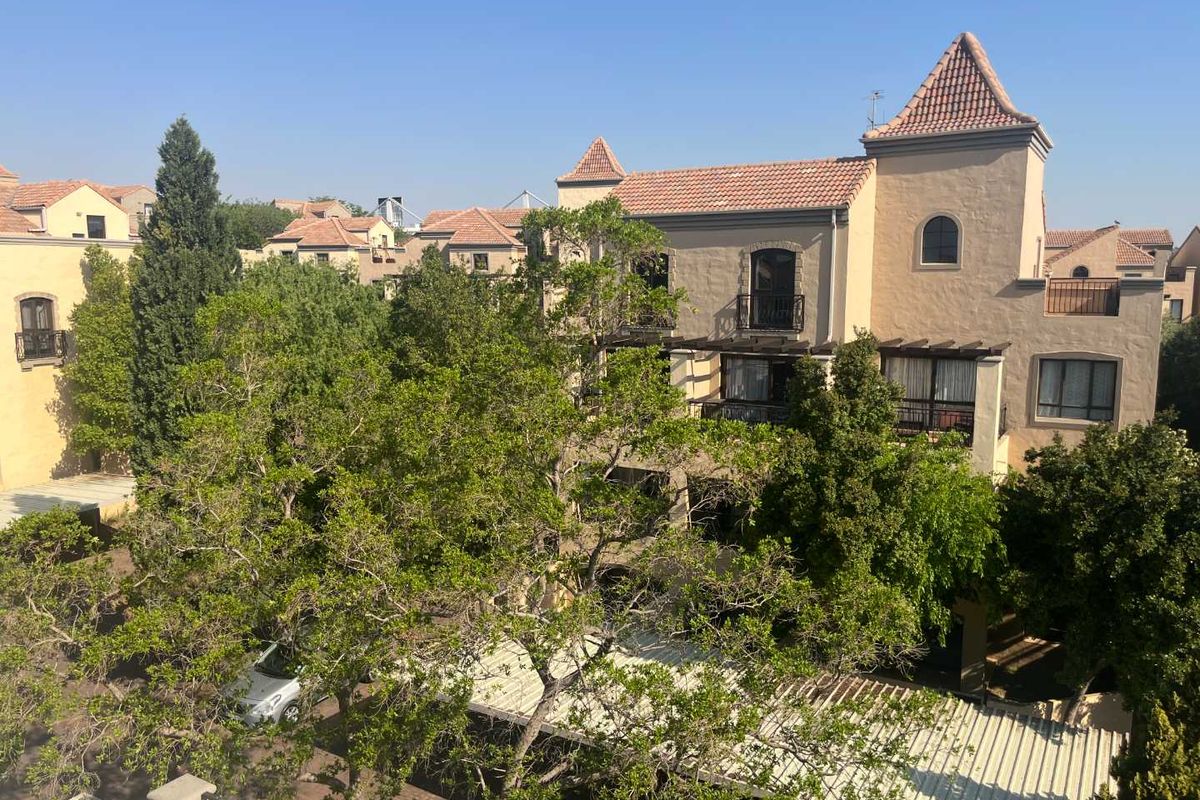 A view of the apartment complex exterior featuring Mediterranean-style architecture with terracotta roof tiles, balconies, and established trees.