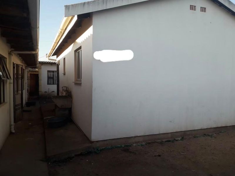 A view of the rear exterior of the house, featuring a concrete wash basin, guttering, and a side pathway with security gate access.