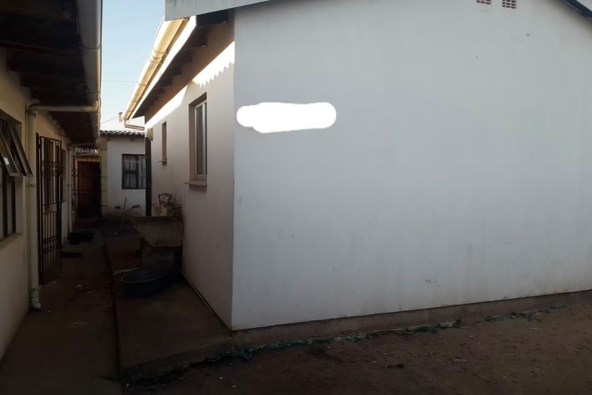 A view of the rear exterior of the house, featuring a concrete wash basin, guttering, and a side pathway with security gate access.