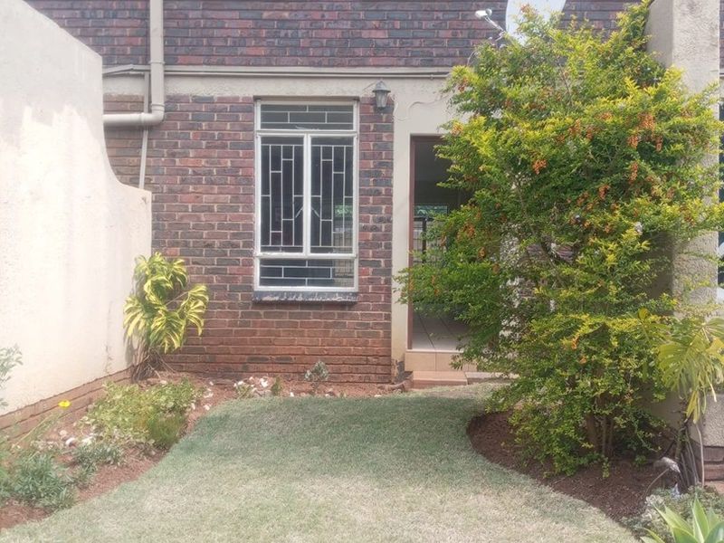 A rear view of a brick apartment building featuring arched windows with security bars, a small private lawn, and a low brick boundary wall.