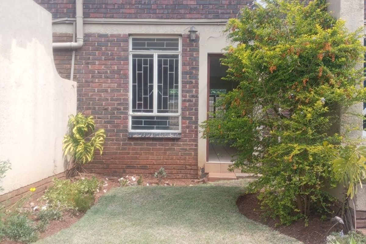 A rear view of a brick apartment building featuring arched windows with security bars, a small private lawn, and a low brick boundary wall.