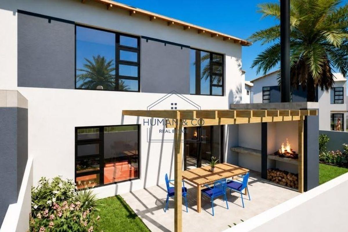 Rear exterior view of the townhouse featuring a paved patio with a wooden pergola and a built-in braai area overlooking a private garden.