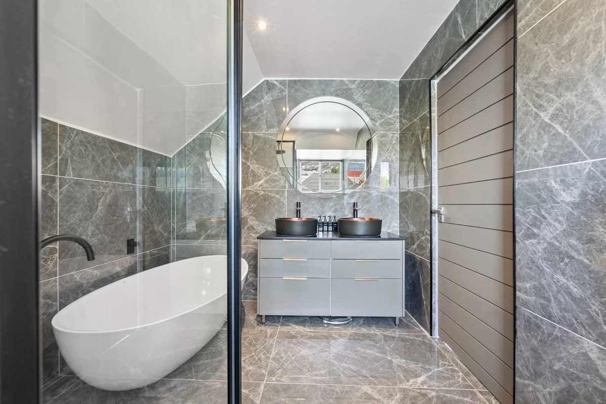 Modern bathroom featuring a freestanding bathtub, glass-enclosed shower, double vanity with vessel sinks, and elegant marble-look tiling throughout.