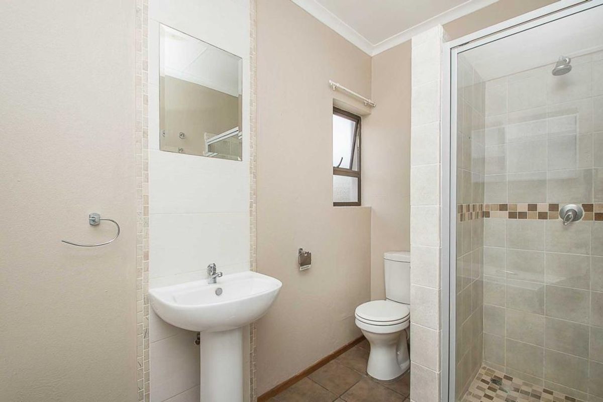 A functional bathroom featuring a pedestal basin, a tiled shower enclosure with a glass door, and a standard toilet.
