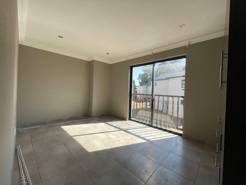 An empty, neutrally painted living area featuring large format floor tiles, recessed lighting, and a sliding glass door leading to a balcony.