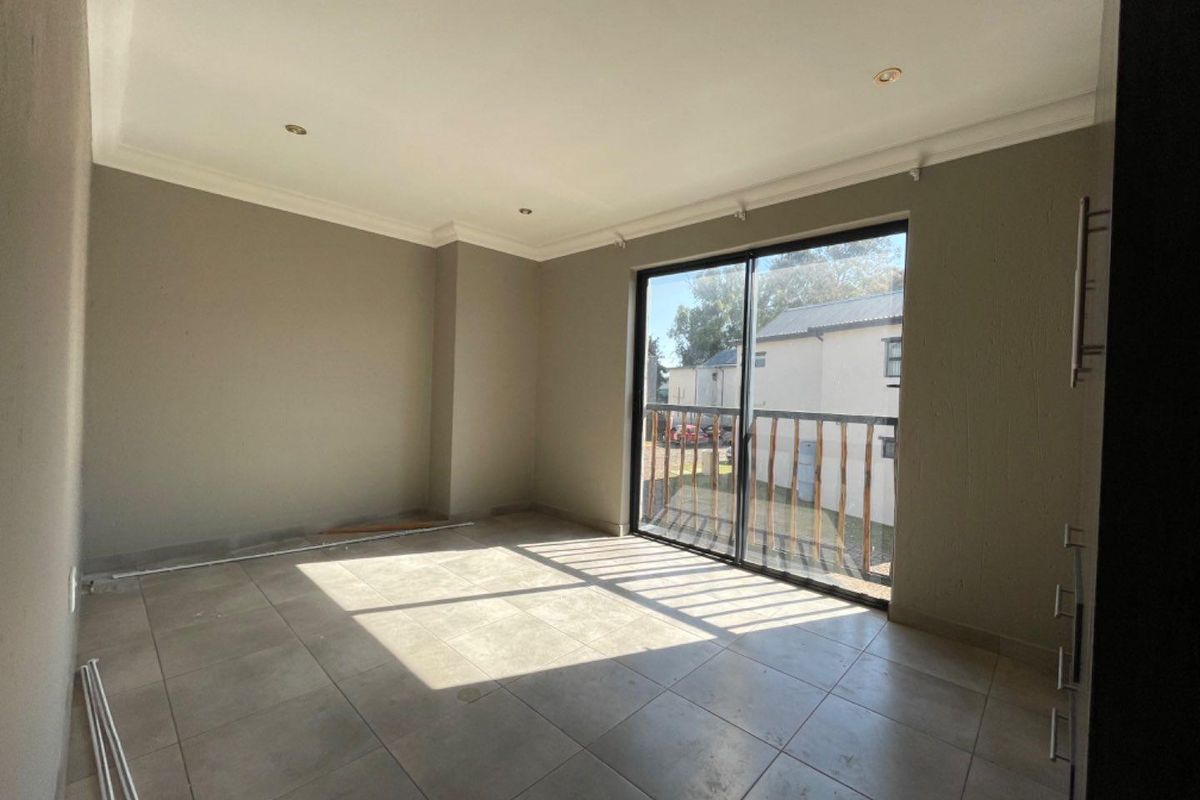 An empty, neutrally painted living area featuring large format floor tiles, recessed lighting, and a sliding glass door leading to a balcony.