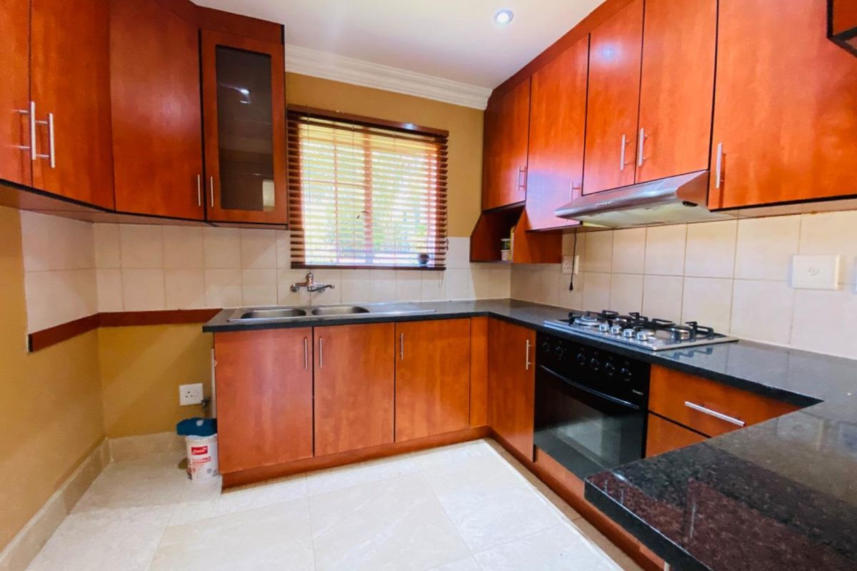A functional kitchen featuring cherry-wood cabinetry, dark granite countertops, a built-in gas hob, oven, and stainless steel extractor fan.