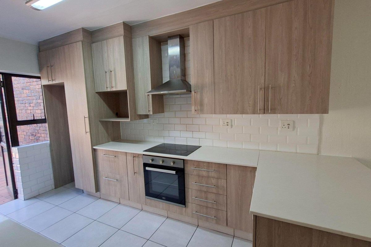 Modern kitchen featuring light wood-finish cabinetry, stone countertops, subway tile backsplash, and integrated stainless steel appliances, with direct access to an outdoor patio area.