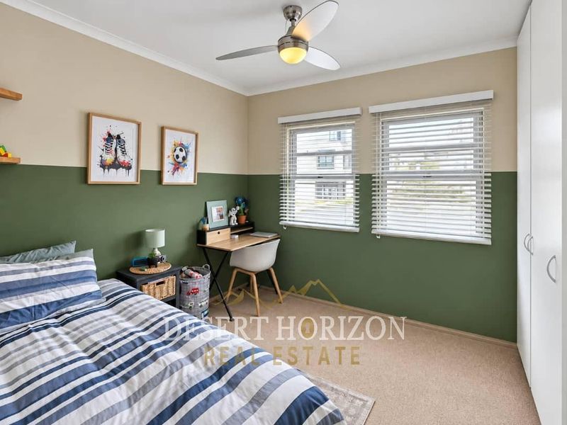 A well-maintained bedroom featuring neutral and green two-tone walls, a ceiling fan, built-in wardrobe storage, and venetian blinds.