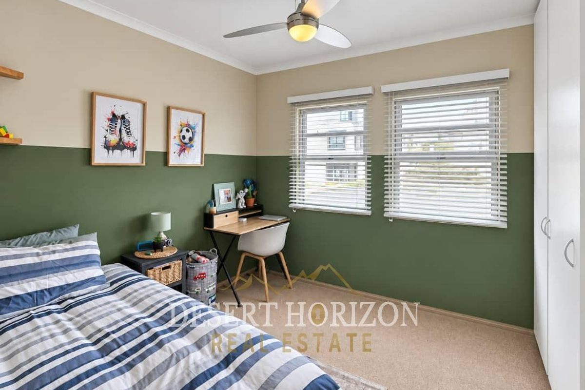 A well-maintained bedroom featuring neutral and green two-tone walls, a ceiling fan, built-in wardrobe storage, and venetian blinds.