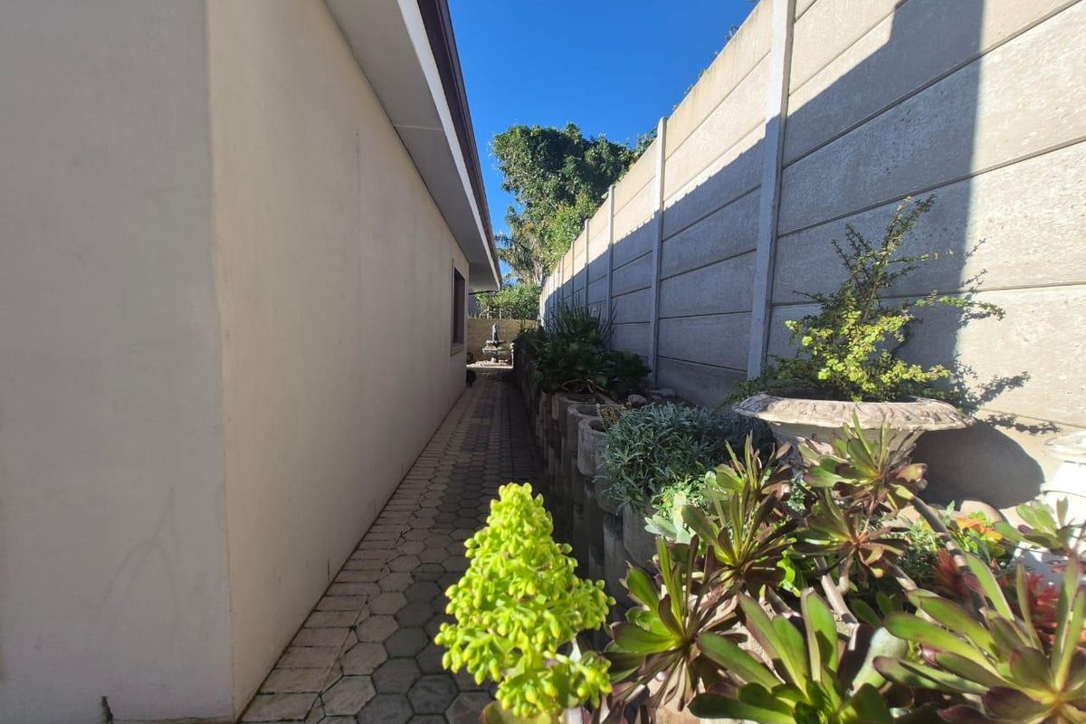 A narrow side passage featuring paved walkway, precast concrete boundary wall, and established garden beds along the side of the house.
