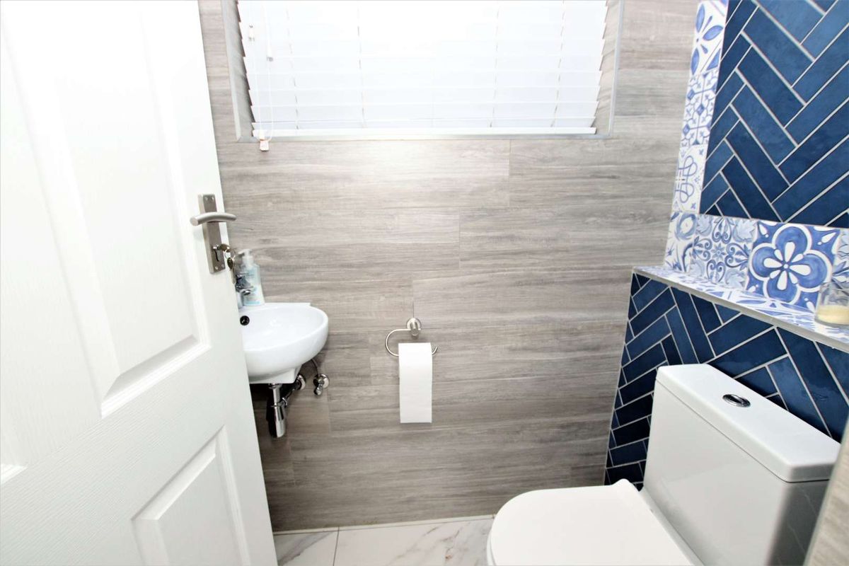 A modern guest bathroom featuring a wall-mounted basin, a toilet, and decorative blue herringbone and patterned tile accents against wood-look wall tiles.