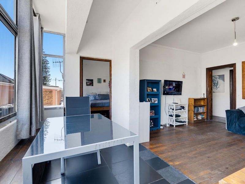 Open plan living area featuring a mix of timber and tiled flooring, large windows providing natural light, and direct access to adjacent rooms.