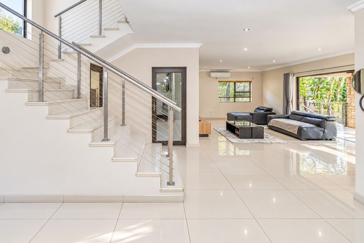 Spacious open-plan living area featuring polished porcelain tiles, a modern staircase with stainless steel balustrades, and direct access to the outdoor patio.
