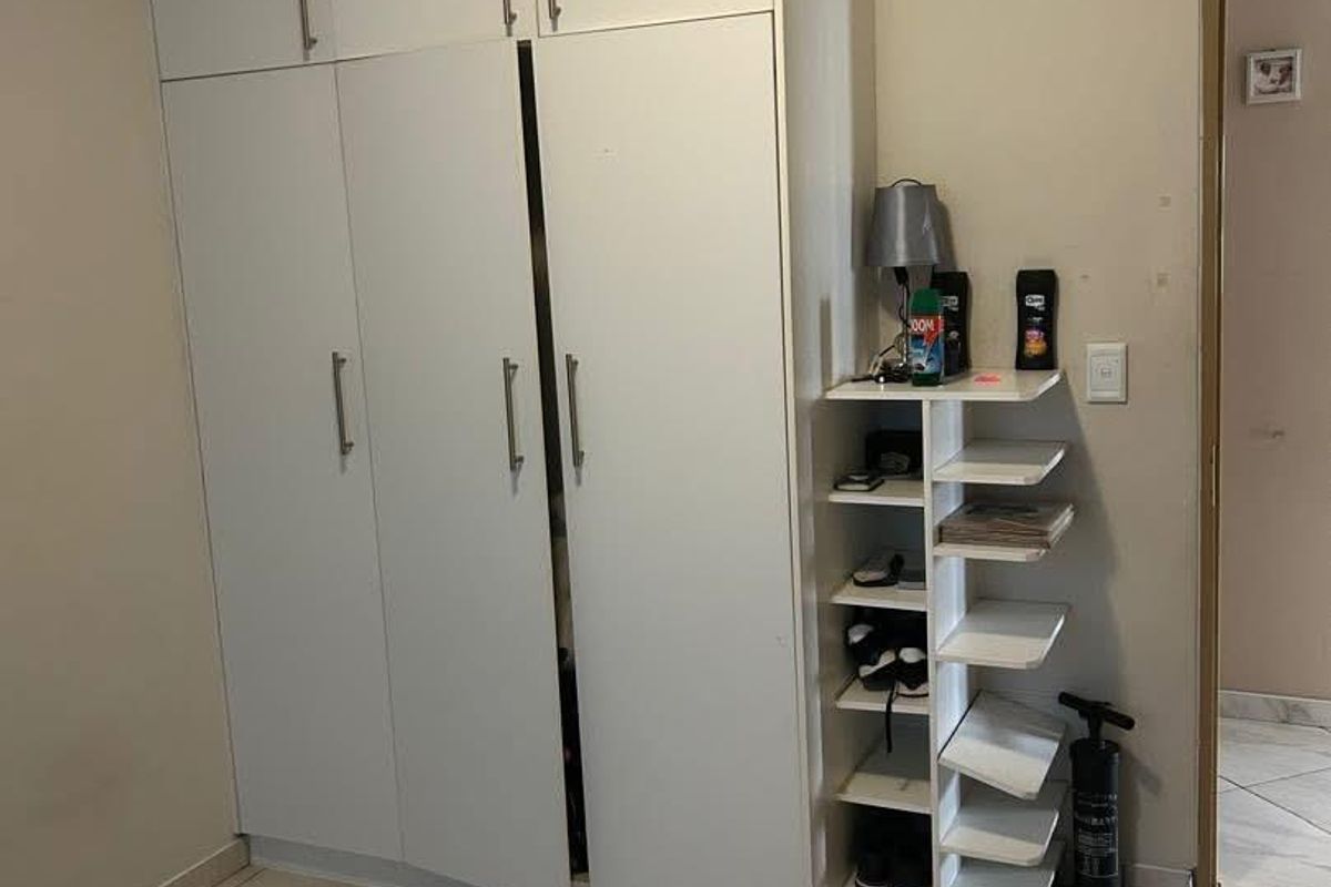 A bedroom featuring white built-in cupboards with modern handles and neutral tiled flooring.