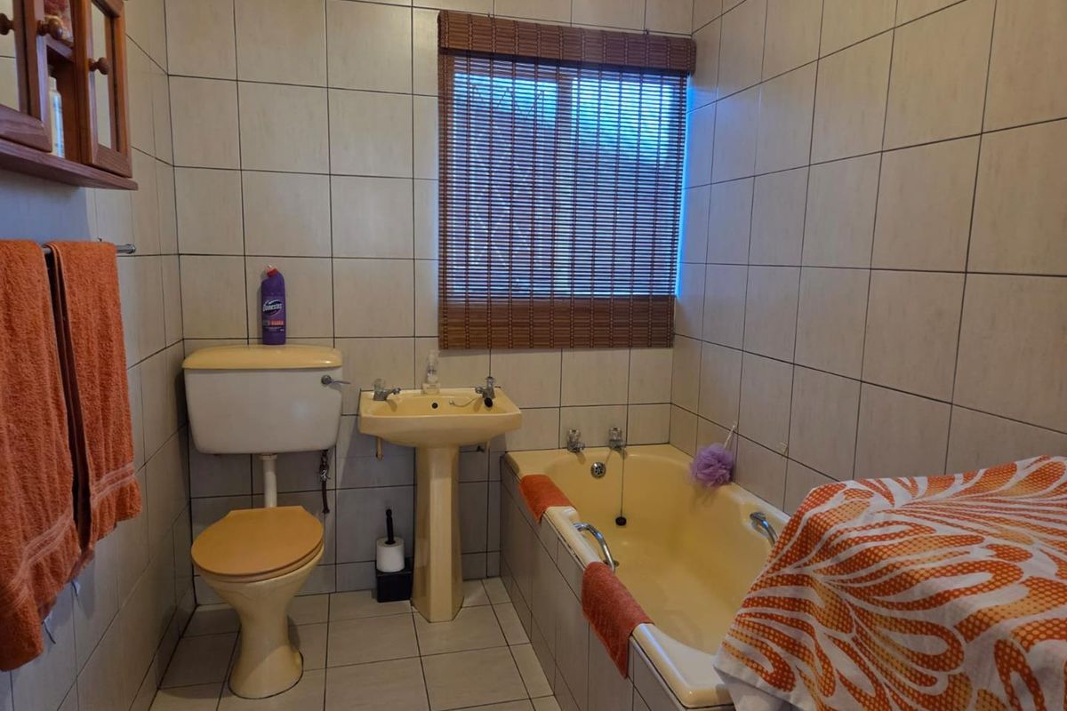 A functional bathroom featuring tiled walls and floor, equipped with a pedestal basin, toilet, and bathtub. The space would benefit from modern updates.