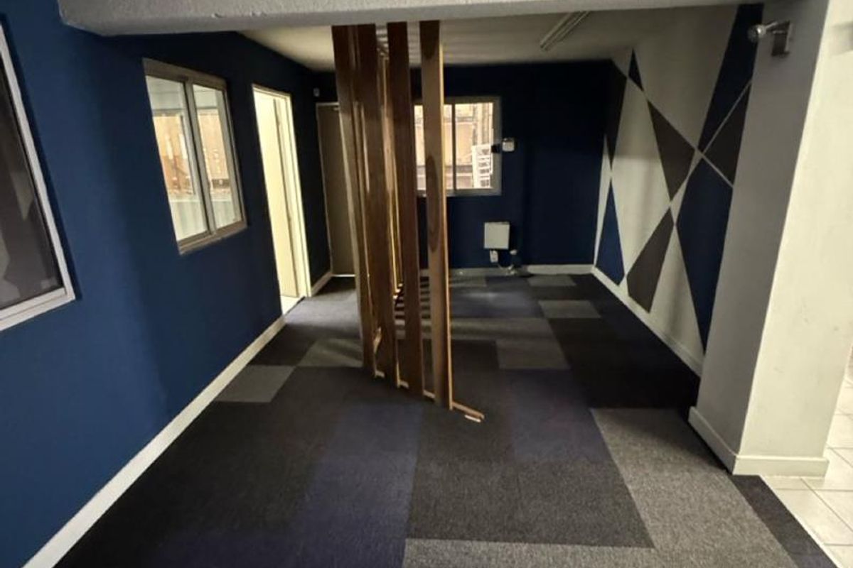 Open plan office space featuring modular carpet tiles, a decorative timber slat divider, and exposed structural beams with modern blue and geometric wall accents.