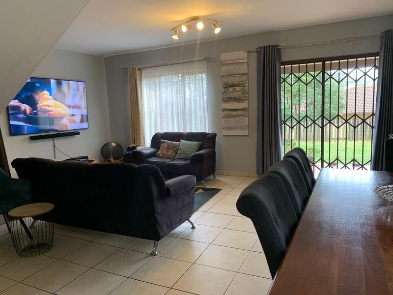 Open plan living and dining area featuring ceramic floor tiles and a sliding glass door with security gate leading to the garden.