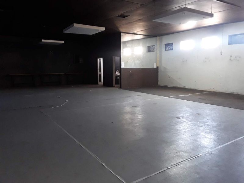 A large, open-plan commercial space featuring high ceilings with recessed lighting, concrete flooring, and a separate restroom area.