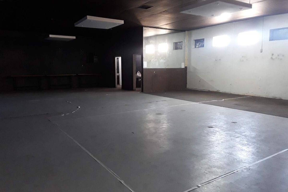 A large, open-plan commercial space featuring high ceilings with recessed lighting, concrete flooring, and a separate restroom area.