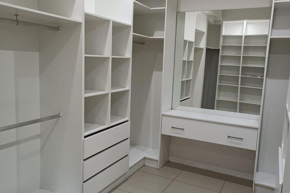 A well-organized walk-in closet featuring extensive built-in cabinetry, shelving, hanging rails, a vanity mirror, and a wall-mounted air conditioning unit.
