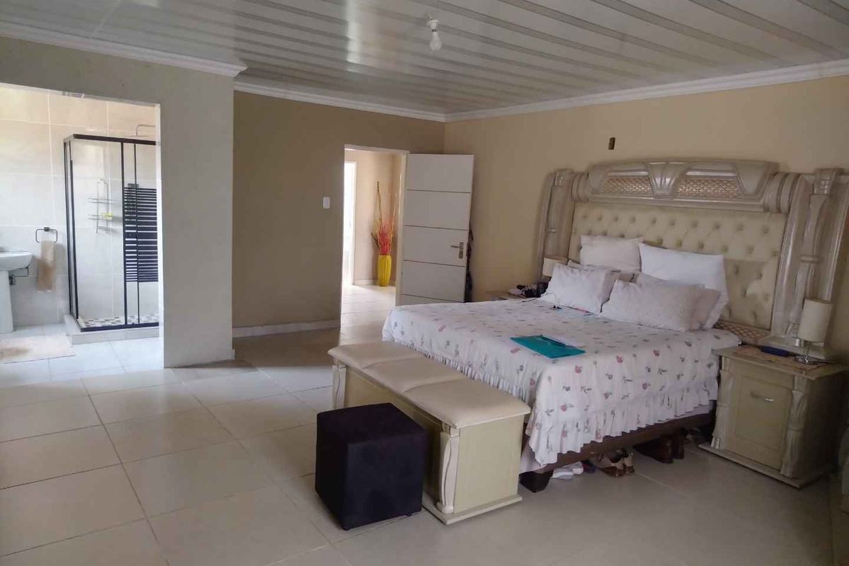 Spacious bedroom featuring tiled flooring, a panelled ceiling, and an integrated en-suite bathroom with a glass-enclosed shower.