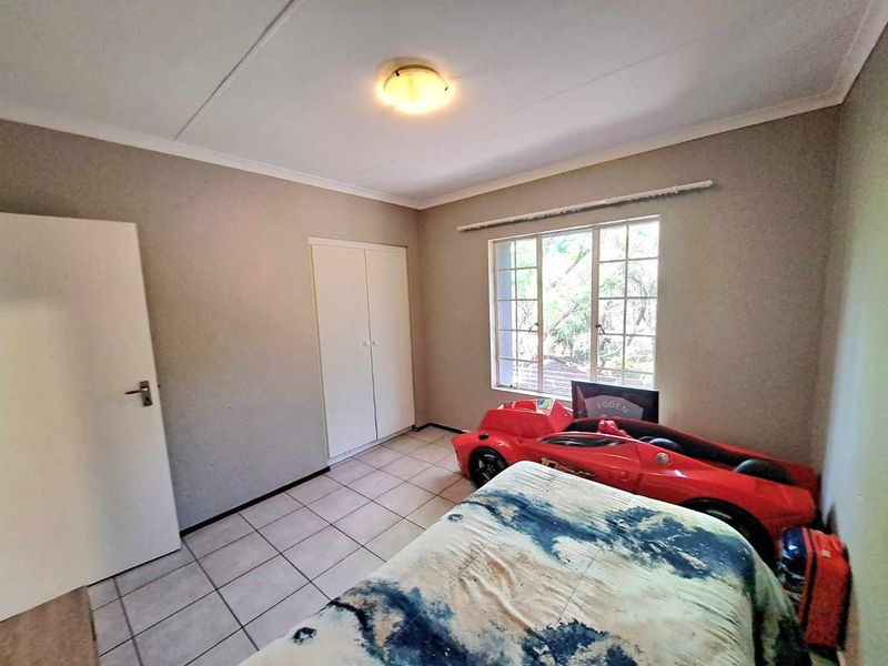 A functional bedroom featuring tiled flooring, built-in cupboards, and a window with security bars, providing a neutral base for personalization.