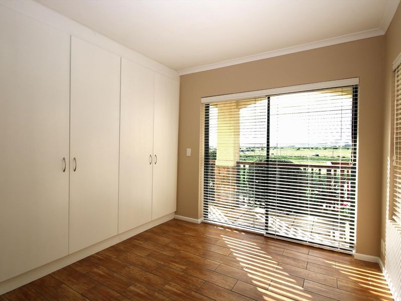 A bright, empty bedroom featuring built-in cupboards, wood-look tiled flooring, and a sliding glass door leading to a balcony with scenic views.