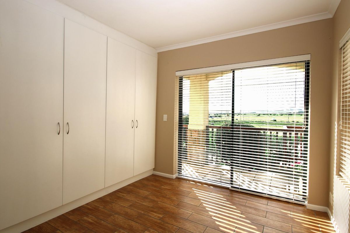 A bright, empty bedroom featuring built-in cupboards, wood-look tiled flooring, and a sliding glass door leading to a balcony with scenic views.