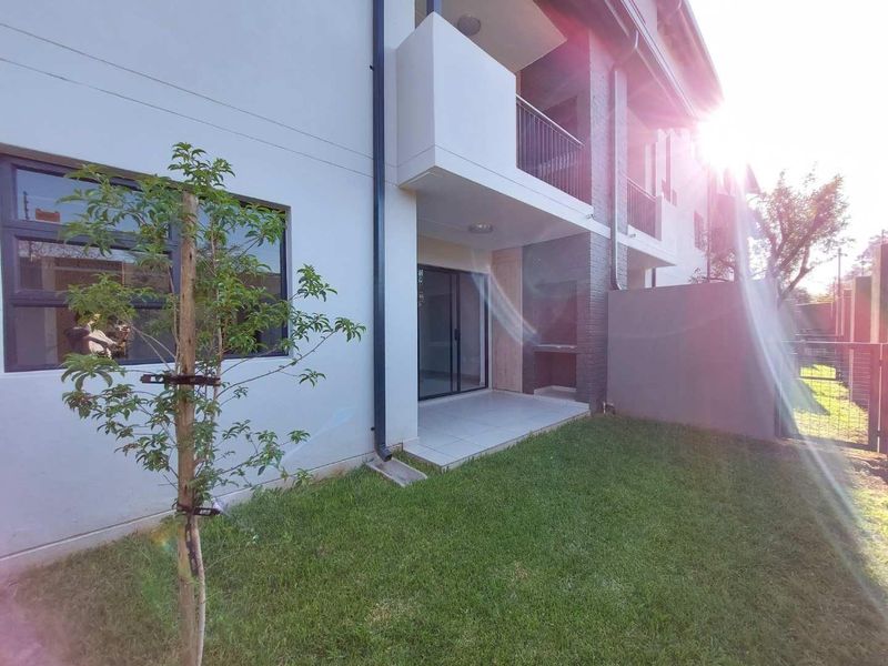 Rear view of the apartment featuring a private garden, tiled patio with a built-in braai, and access via sliding glass doors.