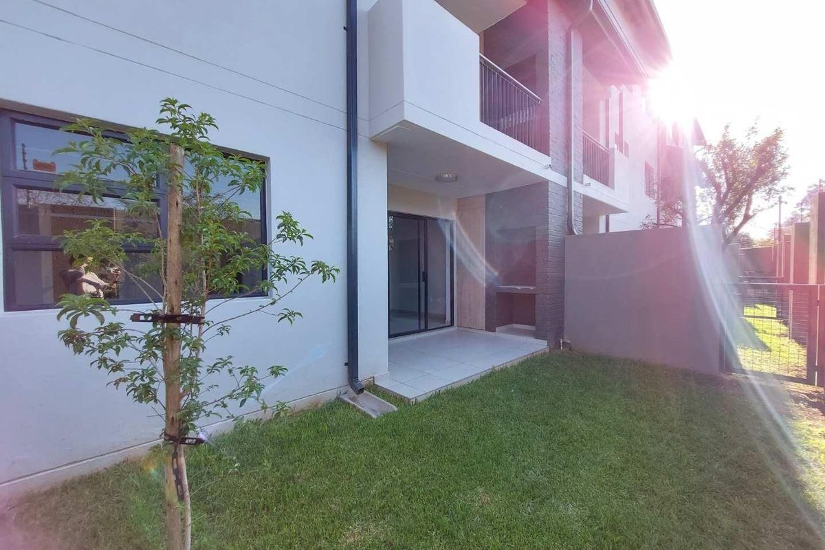 Rear view of the apartment featuring a private garden, tiled patio with a built-in braai, and access via sliding glass doors.