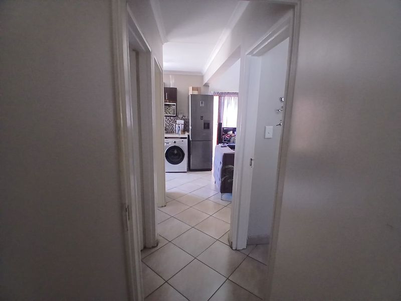 A view through a hallway leading into an open-plan kitchen and living area with tiled flooring throughout.