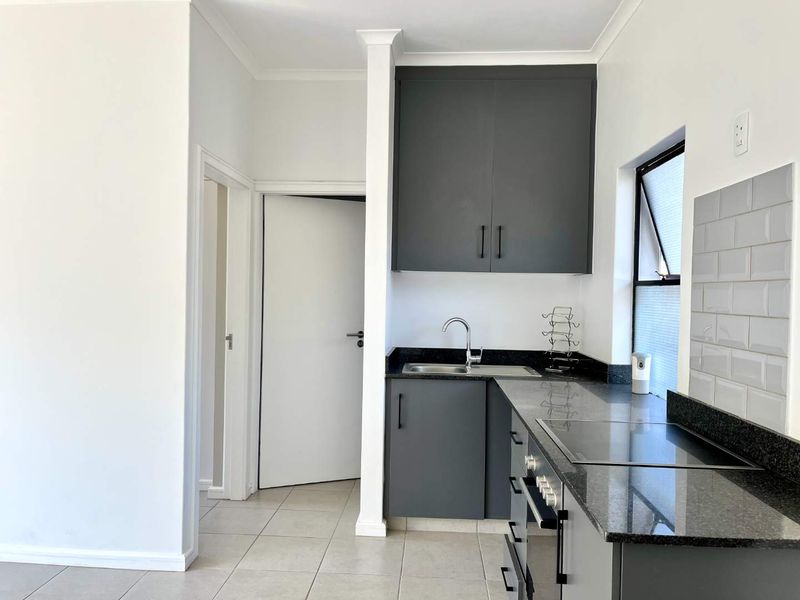 Modern kitchen featuring dark grey cabinetry, granite countertops, subway tile backsplash, and integrated electric hob and oven, set against neutral tiled flooring.