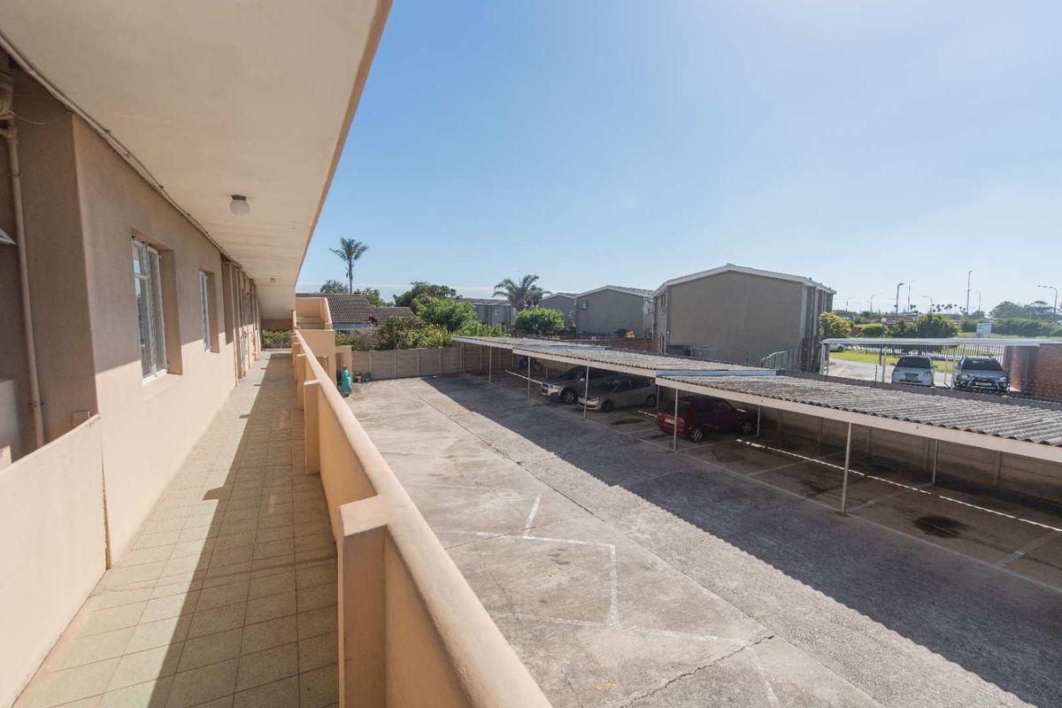 An elevated view from an apartment walkway overlooking the complex parking area with covered carports and concrete paving.