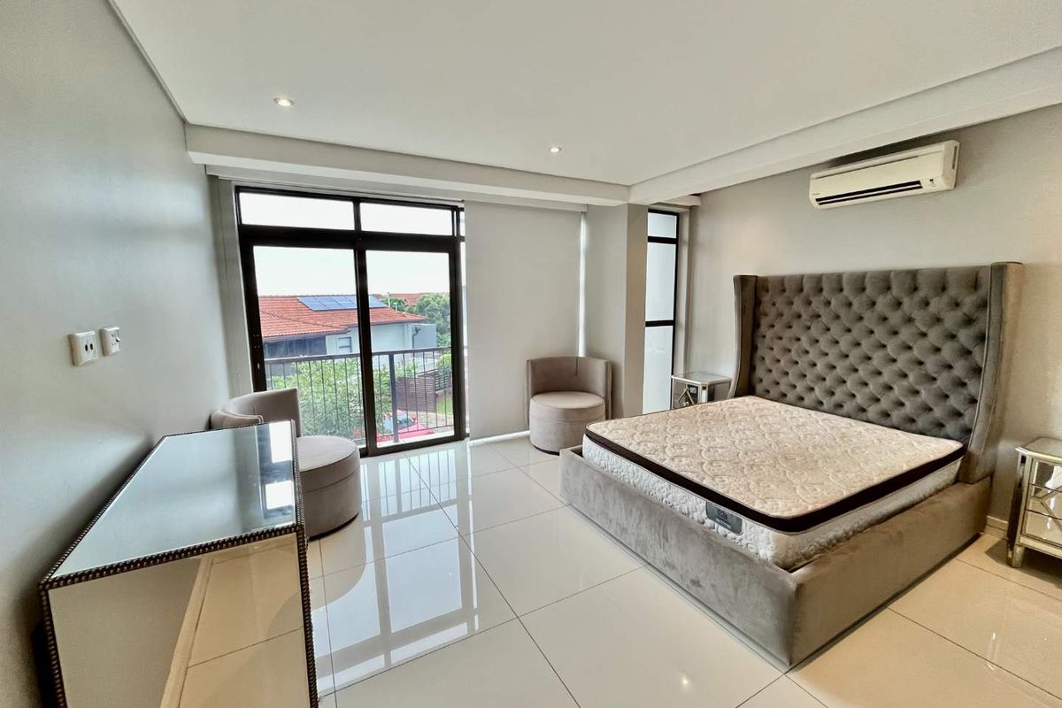 Spacious bedroom featuring polished porcelain floor tiles, recessed downlighting, a wall-mounted air conditioning unit, and sliding glass doors leading to a private balcony.