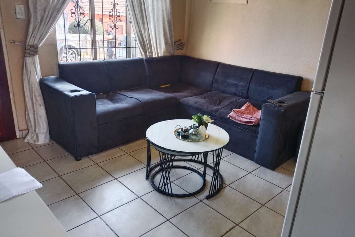 A compact living area featuring ceramic floor tiles and a window with security bars, providing a functional space for relaxation.