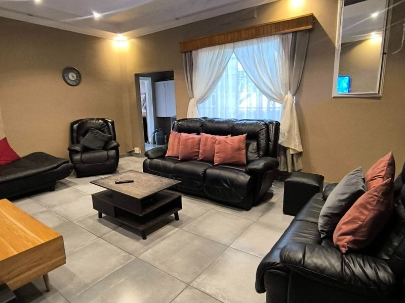 A spacious living room featuring large format floor tiles, a recessed ceiling with integrated downlights, and decorative cornicing.