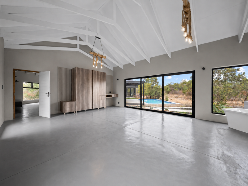 Spacious bedroom featuring vaulted ceilings with exposed rafters, polished concrete floors, built-in cabinetry, and large sliding doors opening to a pool area.