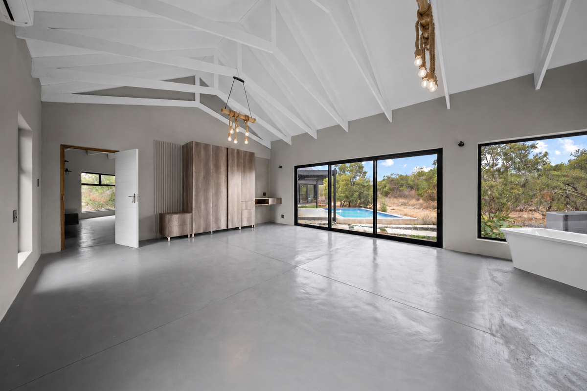 Spacious bedroom featuring vaulted ceilings with exposed rafters, polished concrete floors, built-in cabinetry, and large sliding doors opening to a pool area.